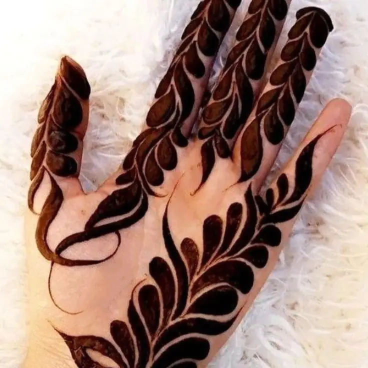 “Hand with bold leafy mehndi design covering fingers and back of the hand on a light background.”